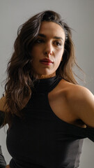 Naklejka premium In a studio setting with a white background, a young black-haired woman wearing a black blouse and jeans strikes an artistic pose