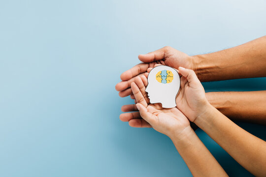 Hands holding a brain jigsaw in a head paper cut symbolize Down Syndrome awareness. - Powered by Adobe