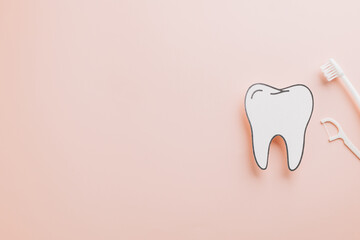 Dentist Day awareness. Toothbrush, floss, and paper tooth model on pink background
