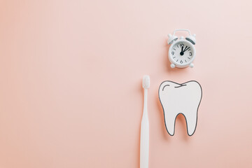 Dentist Day highlights. Paper tooth, toothbrush, and white alarm clock on pink background