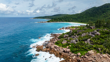Rocky coast lined with dense greenery and tropical plants by the ocean. La Digue, Seychelles.