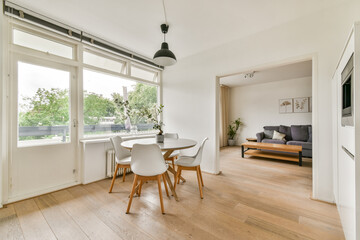 A stylish and bright modern dining area featuring a round table, white chairs, and large windows, blending comfort with minimalism for a refreshing atmosphere.