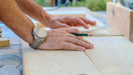 A middle-aged man measures with a tape measure to make repairs with lumber in his garden on a...