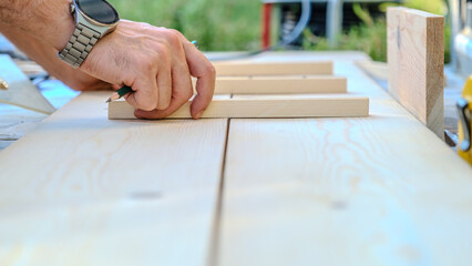 A middle-aged man measures with a tape measure to make repairs with lumber in his garden on a...