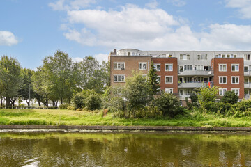 A picturesque view of a residential apartment building set against a backdrop of lush greenery and a serene water body, inviting tranquility and nature.