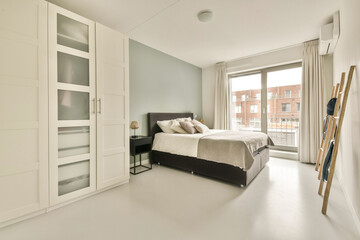 A spacious modern bedroom featuring neutral colors, large windows, and sleek furniture. The room emphasizes simplicity with a cozy atmosphere.