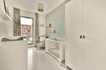 A stylish baby room featuring minimalistic decor, a crib, and ample natural light. The soft color palette and modern furniture create a cozy atmosphere.