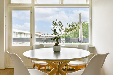 A spacious dining area featuring a round table and chairs, complemented by large windows offering a beautiful view of greenery and the sky, enhancing the ambiance.