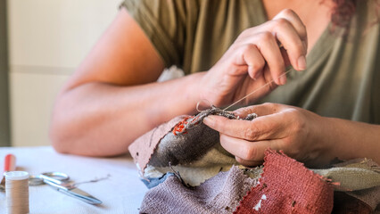 A close-up image of the hands of a middle-aged woman sewing a bag with needle and thread while sitting at home