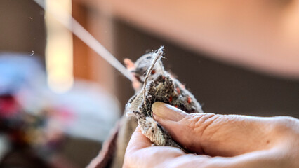 A close-up image of the hands of a middle-aged woman sewing a bag with needle and thread while sitting at home
