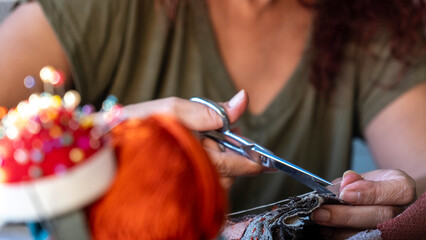 A close-up image of the hands of a middle-aged woman sewing a bag with needle and thread while...