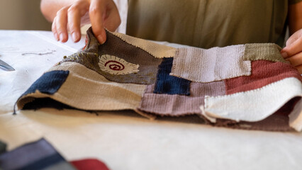 A close-up image of the hands of a middle-aged woman sewing a bag with needle and thread while sitting at home