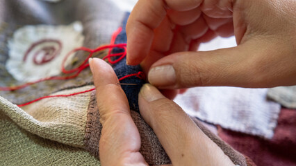 A close-up image of the hands of a middle-aged woman sewing a bag with needle and thread while...