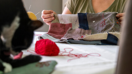 A close-up image of the hands of a middle-aged woman sewing a bag with needle and thread while...