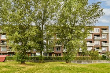 A serene view of modern residential buildings framed by lush green trees, showcasing a blend of urban living and nature. The surrounding grass offers a vibrant touch.