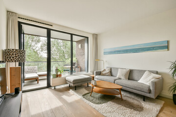 A stylish modern living room featuring a neutral sofa, natural light through large windows, and cozy decor elements that create a welcoming atmosphere.