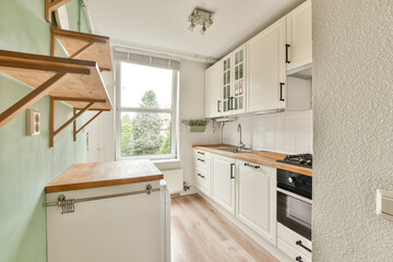 A sleek kitchen with white cabinetry, a wooden countertop, and large windows that invite natural light, creating a warm and inviting atmosphere.