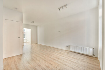 A bright and spacious modern interior featuring light-colored wooden flooring and simple design elements. The room is empty, highlighting its clean lines.
