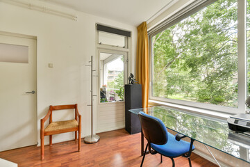 A minimalist workspace featuring a glass desk and a chair, surrounded by large windows that let in natural light, enhancing the inviting atmosphere.