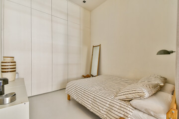 A serene and modern bedroom showcasing a simple design with a bed, striped bedding, a mirror, and clean lines, emphasizing tranquility and comfort.
