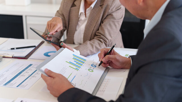 Senior executives collaborating on business strategy using a tablet to analyze financial data and company performance in a meeting.