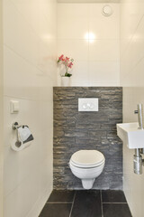 A contemporary bathroom featuring a toilet, a small sink, and a decorative stone wall with a floral element. The design combines sleek lines with natural accents.