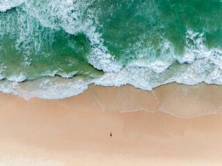 aerial top view of the sea waves hitting the beach, tourists play in the sea and sunbathing on the sand beach at surin beach phuket thailand,