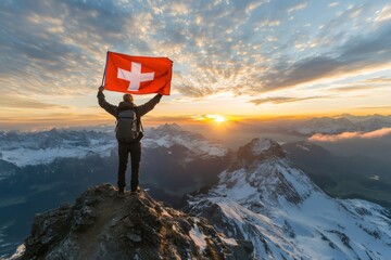 Obraz premium Hiker is holding Swiss flag on top of a mountain at sunrise