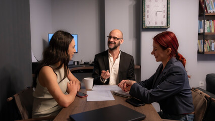 A businessman and two business women, dressed in office attire, having a meeting in the office with a computer in front of them.