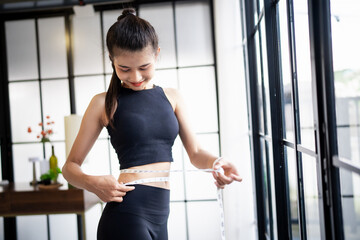 Asian healthy woman dieting Weight loss. Slim woman measuring waist with measure tape after diet at...