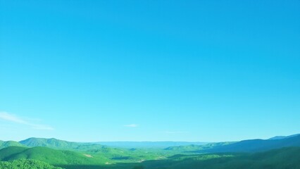 Obraz premium A vast landscape of lush green hills under a clear spring blue sky.