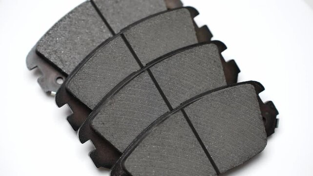 Row of four brake pads neatly stacked on top of each other, on white background, rotating on turntable. Auto parts replacement concept, car maintenance, brake system health