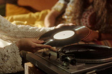 Closeup of hands placing vinyl record on turntable in cozy, vintage-inspired room with warm...