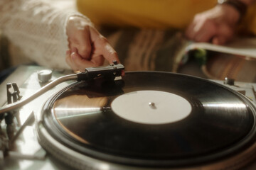Hand gently placing needle on vinyl record on vintage record player, capturing nostalgic atmosphere with cozy background setting