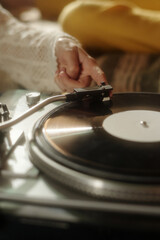 Close-up of hand placing needle on vinyl turntable while preparing to play a record, focusing on detail and texture, with ambient lighting creating a warm atmosphere