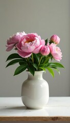 Simple ceramic vase with peony flowers and greenery on a neutral-colored table, rustic, clean