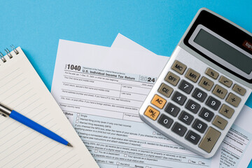 Top view of tax forms, calculator and pen on blue table