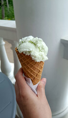 Delicious pistachio ice cream in a waffle cone, held in hand.