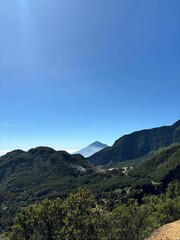 A clear blue sky overlooks green mountains and peaks in the distance