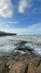 The rocky shoreline alongside ocean waters under a cloudy blue sky