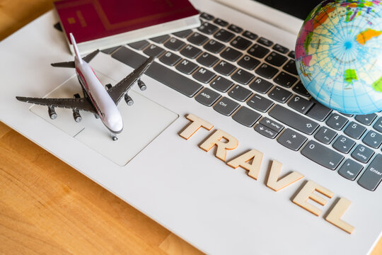 Airplane model, passport, globe and wooden letters spelling travel are laying on laptop keyboard suggesting online booking and vacation trip planning - Powered by Adobe
