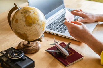 Traveler is booking a flight using a laptop and a credit card, with a globe, passport, toy airplane, and vintage camera on the table, symbolizing travel planning and wanderlust