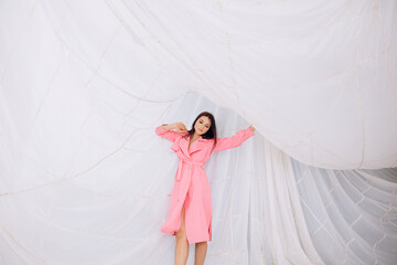 Beautiful adult young female model in the studio on the background of a parachute in a pink coat