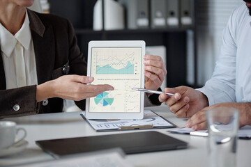 Close up of unrecognizable woman pointing at statistics graph on tablet screen while sitting at...
