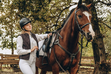 Obraz premium A young female equestrian stands near her horse and prepares for a competition.
