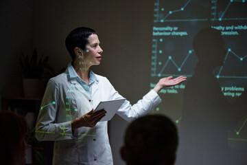 Side view portrait of professional female scientist giving presentation on stage and pointing at data projections, copy space