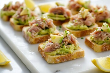 Minimalistic presentation of mini toasts on a sleek white marble plate, topped with mashed avocado, chunks of canned tuna, and a splash of lemon juice. The clean lines and vibrant colors stand out.