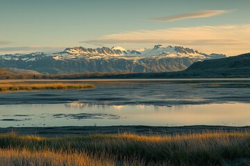 Obraz premium Tranquil Natural Scenery with Majestic Snow-Capped Mountains, Reflective Lake, and Golden Meadow. A Harmonious and Peaceful Landscape with Clear Sky and Leisurely Clouds