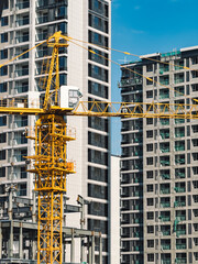 A tall yellow construction crane stands between modern high-rise buildings
