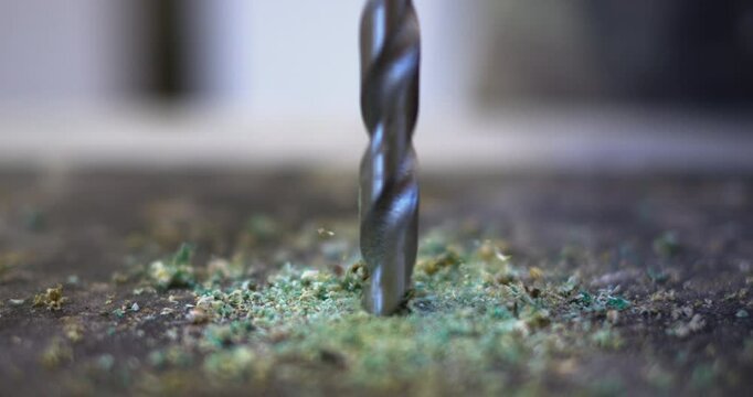 The drill drills into the surface of the countertop, producing green shavings.